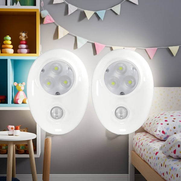 Two motion sensor night lights on a wall in a child's bedroom with toys and a bed in the background.