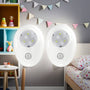 Two motion sensor night lights on a wall in a child's bedroom with toys and a bed in the background.