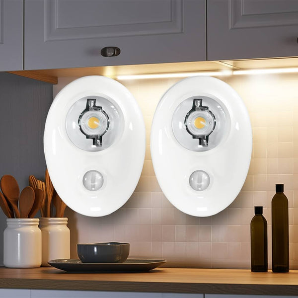 Two motion sensor lights mounted on a kitchen wall with cabinets and utensils in the background.