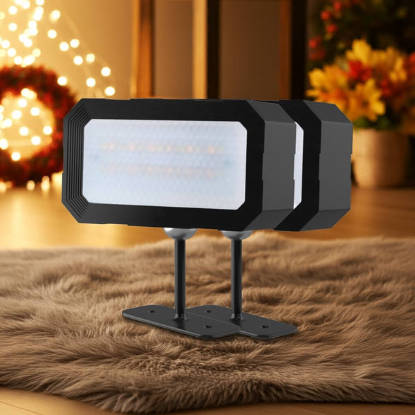 Two black outdoor flood lights on a fur surface with decorative lights and flowers in the background.